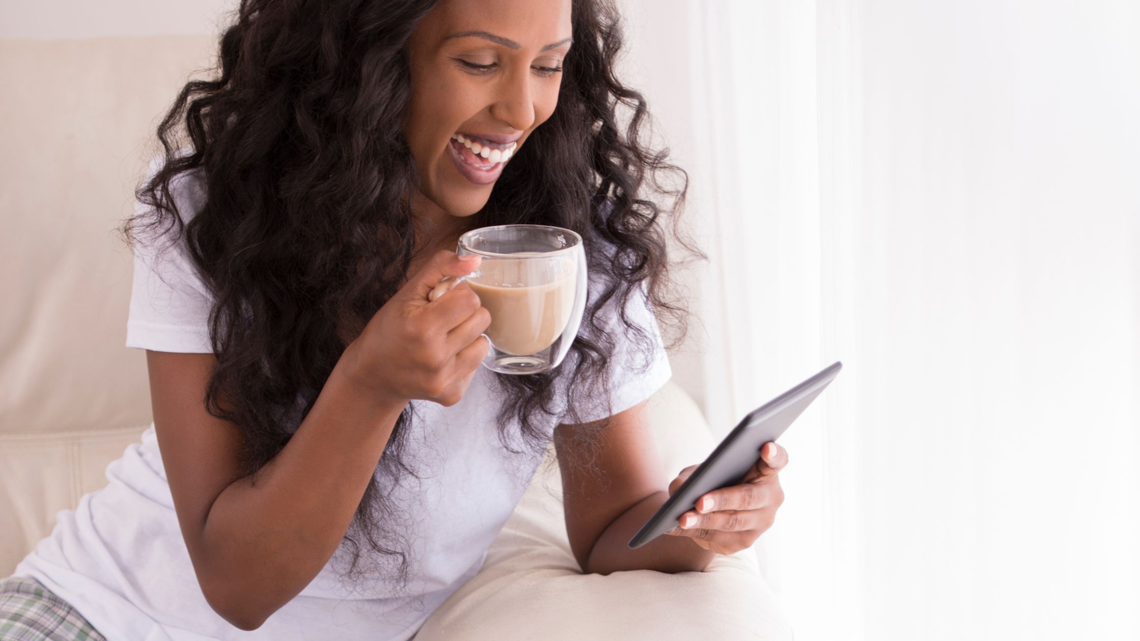 Una mujer con una taza en la mano y sonriendo mientras mira el móvil